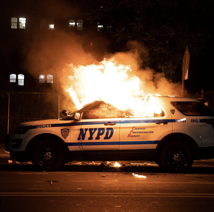 An NYPD police SUV on fire on a city street at night