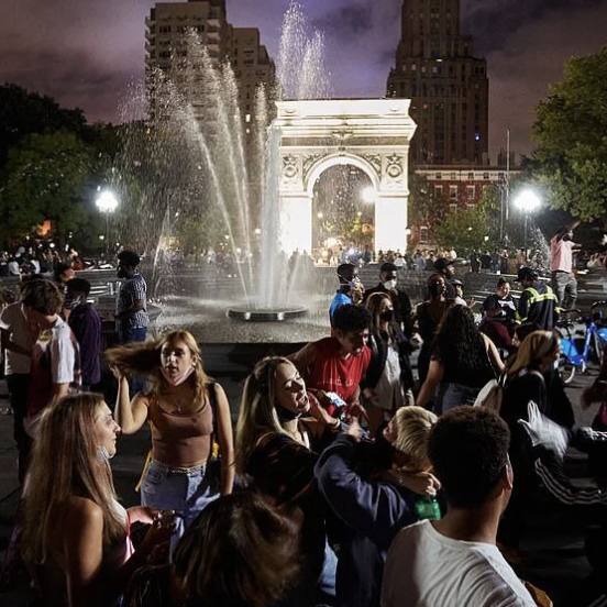A crowded Washington Square Park at night in warm weather, with people gathered around the fountain